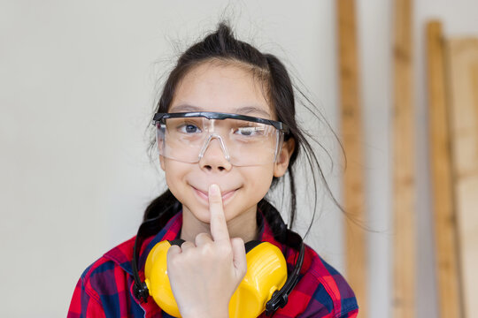 Asian girl standing with noise reduction earmuffs makes funny face in a carpentry workshop