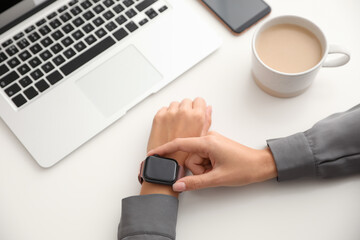 Woman checking stylish smart watch at table, closeup