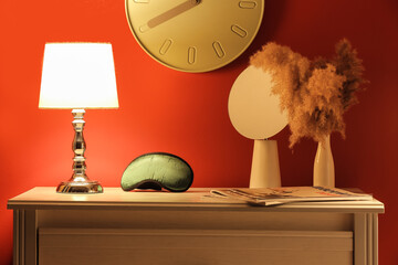 Stylish sleeping mask and lamp on shelf in room