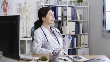 pretty physician taking a break from work is turning to look outside the window on the swivel chair...