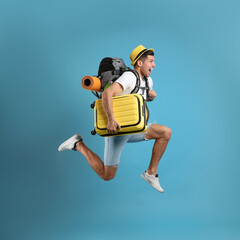 Emotional male tourist with travel backpack and suitcase jumping on turquoise background