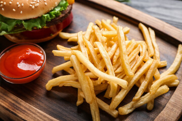 Tasty french fries, tomato sauce and burger on wooden board