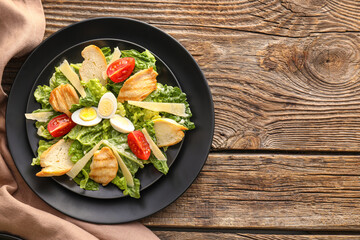 Plate with tasty Caesar salad on wooden background