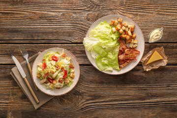 Plates with tasty Caesar salad and sauce on wooden background