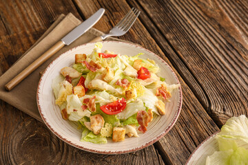Plate with tasty Caesar salad on wooden background