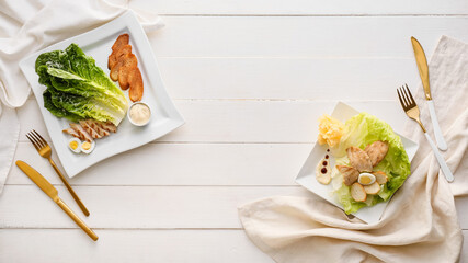 Plates with tasty Caesar salad on light wooden background