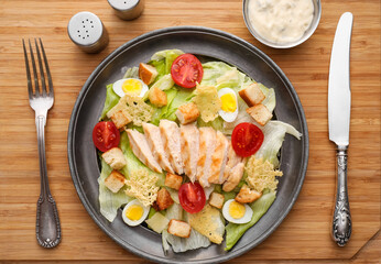 Plate with tasty Caesar salad on wooden board