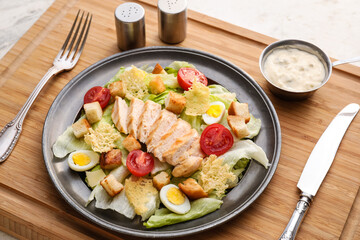 Plate with tasty Caesar salad and sauce on light background