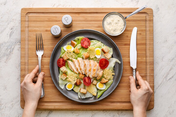 Woman with tasty Caesar salad and sauce on light background