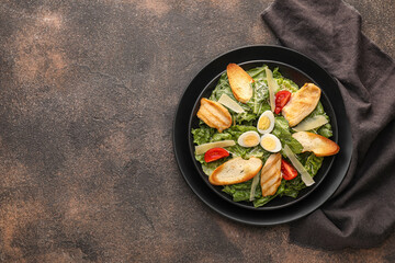 Plate with tasty Caesar salad on grunge background