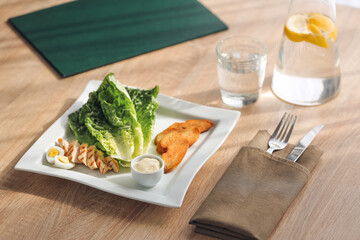 Plate with tasty Caesar salad and sauce on wooden table
