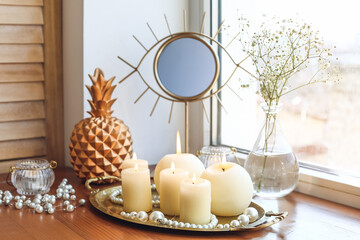 Burning candles with mirror and decor on windowsill