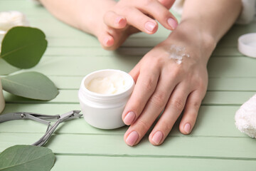 Woman applying shea butter onto hands on color wooden background