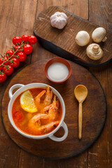 Tom yam soup with shrimps and coconut milk on the table on a round board next to coconut milk and tomatoes.