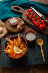 Tom yam soup with shrimps and coconut milk on a table on a black board and a spoon.