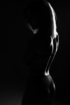 Beautiful female silhouette in lingerie black and white photo. Woman posing on black background
