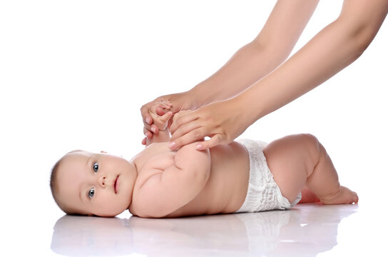 Infant Child Baby Girl Kid In Diaper Is Lying On Her Back, Head Turned To Camera, Ready To Do, Start Exercises To Strengthen Back, Neck, Abdominals Muscles With Her Adult Coach On A White Background