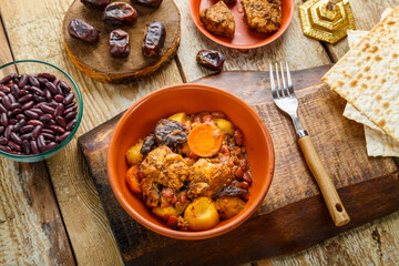 Jewish dish chelnt with meat on a stand next to matzo and ingredients.