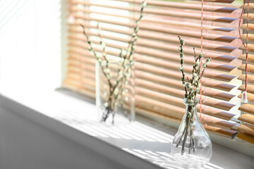 Vases with willow branches on windowsill in room