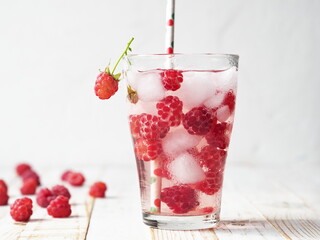 Summer drink with ice, raspberries and tonic. A glass on a light wooden background.
