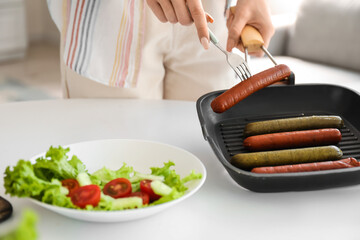 Young woman with tasty sausages and vegetable salad in kitchen