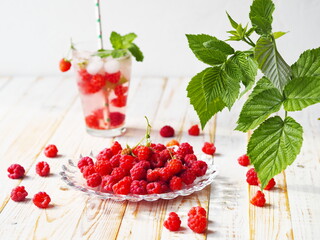 Summer drink with ice, raspberries and tonic. A glass on a light wooden background.