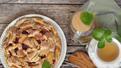Autumn homemade charlotte fruit pie on a wooden ancient natural table with tea, teapot and mint. Apples and plum.Place for text.