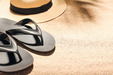 Stylish hat and flip-flops on sand