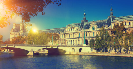 Naklejka premium View of Pont du Carrousel across Seine river leading to arched entrance to Louvre palace courtyard, Paris, France..