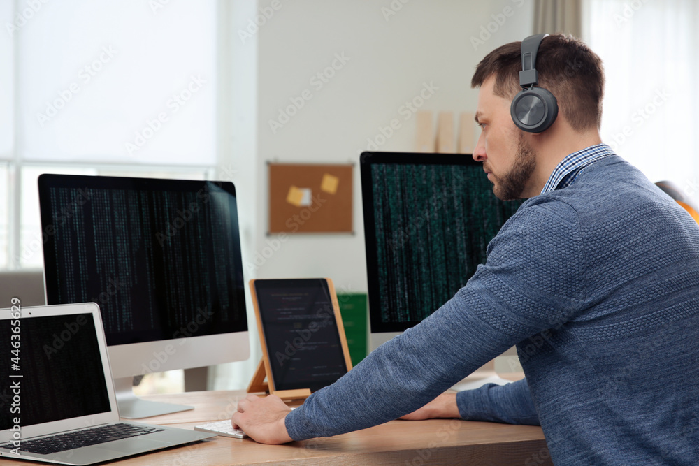 Poster programmer with headphones working at desk in office