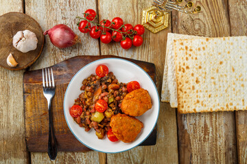 Cod cutlets with stewed potatoes and vegetables on a plate next to matzo and ingredients.