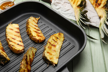 Frying pan with grilled pineapple slices on color wooden background, closeup