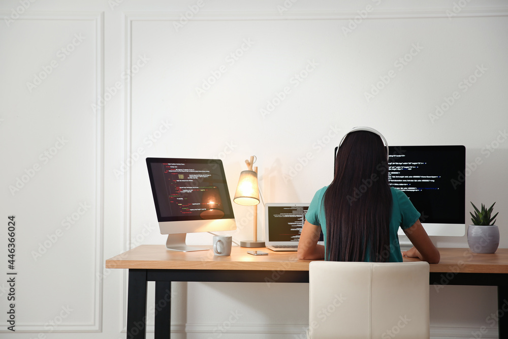 Poster programmer with headphones working at desk in office