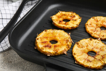Frying pan with grilled pineapple slices on grunge background, closeup