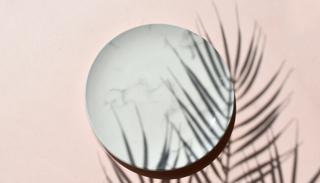 Mockup empty marble plate on neutral beige background. Summer minimal tableware composition. Palm leaves shadow. Elegant concept for wedding invitation, restaurant menu or spa branding.