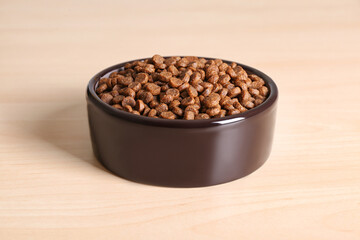 Dry dog food in pet bowl on wooden surface