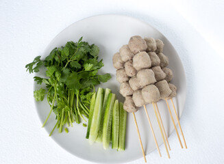 Meatballs on skewers, meatballs, noodles with vegetables, and a cup of dipping sauce put on a plate and white background