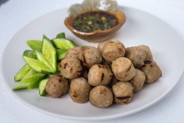 Grilled meatballs, skewers, meatballs, noodles with vegetables and dipping sauces burnt on plate and white Asian food.