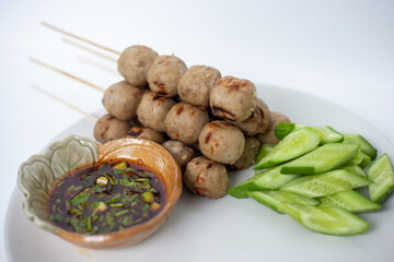 Grilled meatballs, skewers, meatballs, beef noodles with vegetables and dipping sauces burnt on a plate, and white Asian food.