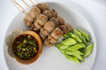 Grilled meatballs, skewers, meatballs, noodles with vegetables and dipping sauces burnt on plate and white Asian food.