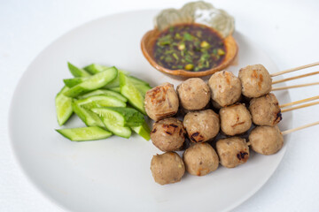 Grilled meatballs, skewers, meatballs, beef noodles with vegetables and dipping sauces burnt on a plate, and white Asian food.