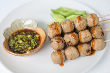 Grilled meatballs, skewers, meatballs, beef noodles with vegetables and dipping sauces burnt on a plate, and white Asian food.