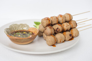 Grilled meatballs, skewers, meatballs, noodles with vegetables and dipping sauces burnt on plate and white Asian food.
