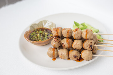 Grilled meatballs, skewers, meatballs, beef noodles with vegetables and dipping sauces burnt on a plate, and white Asian food.