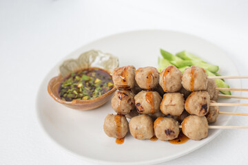 Grilled meatballs, skewers, meatballs, beef noodles with vegetables and dipping sauces burnt on a plate, and white Asian food.