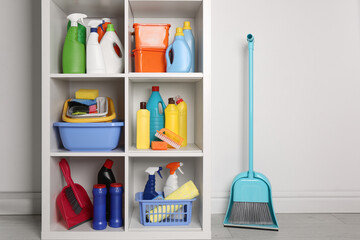 Shelving unit with detergents and cleaning tools near white wall indoors