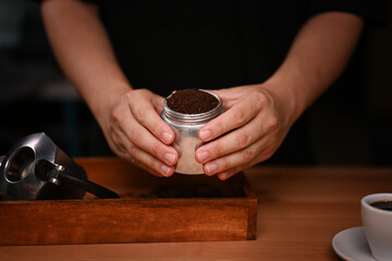 Barista holding moka pot with  ground coffee in dark room.