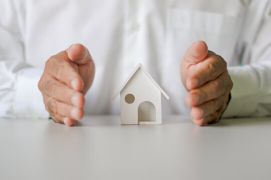 Businessman's hands to protect the safety of homes. Architecture, safety, security, real estate and property concept - close up of hands protecting house or home model.