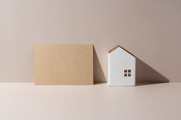 A model of a house on a beige background and a card with nothing written on it.