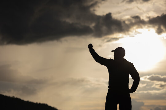 Silhouette Young man raised hand in the air with success goal on sunset background. Man standing on top of the mountain freedom life concept.